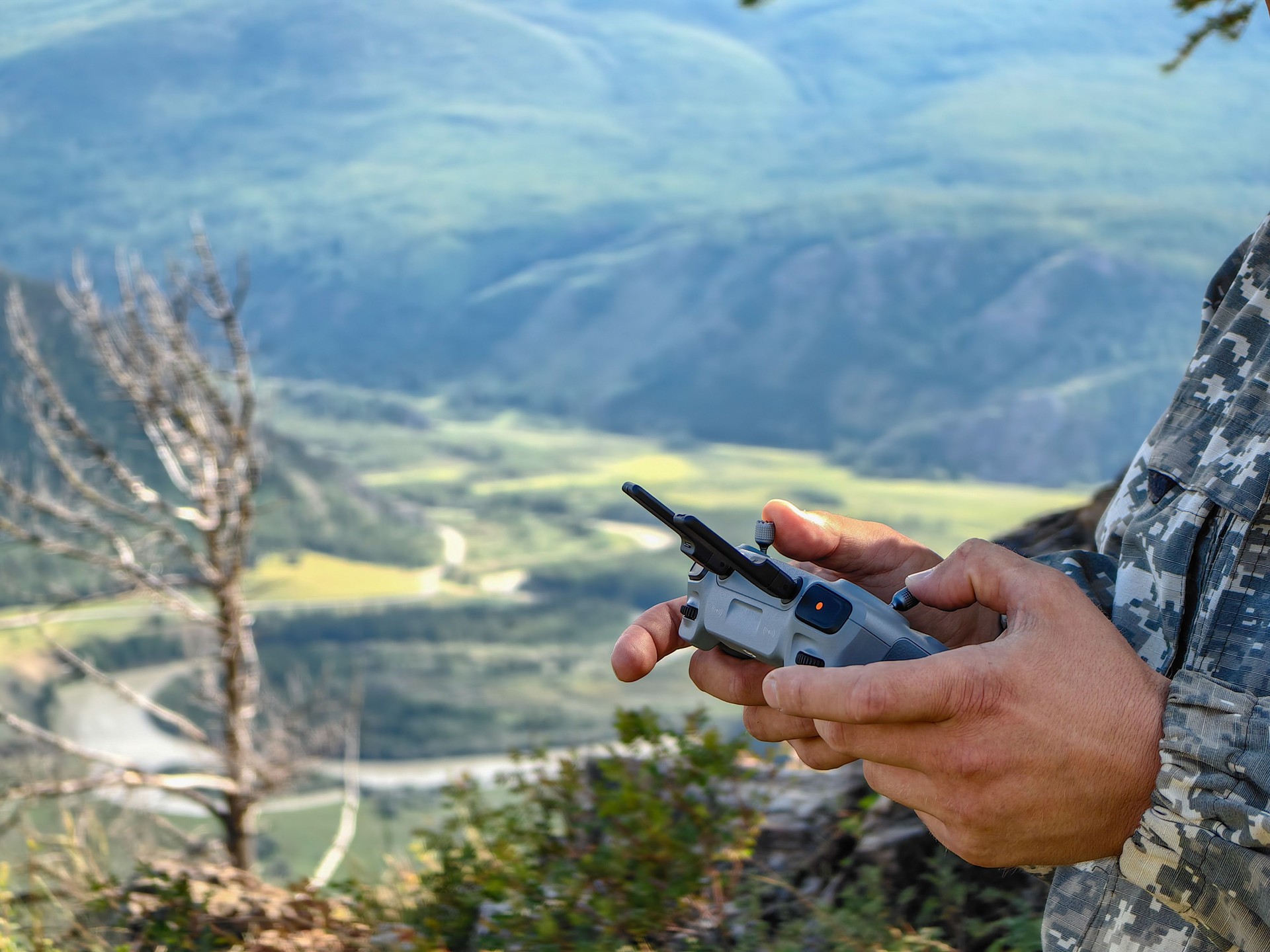 Man uses a remote control to operate a drone in a scenic mountain landscape.
